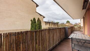 A wooden deck with a table and chairs, a wooden fence, and a building in the background.
