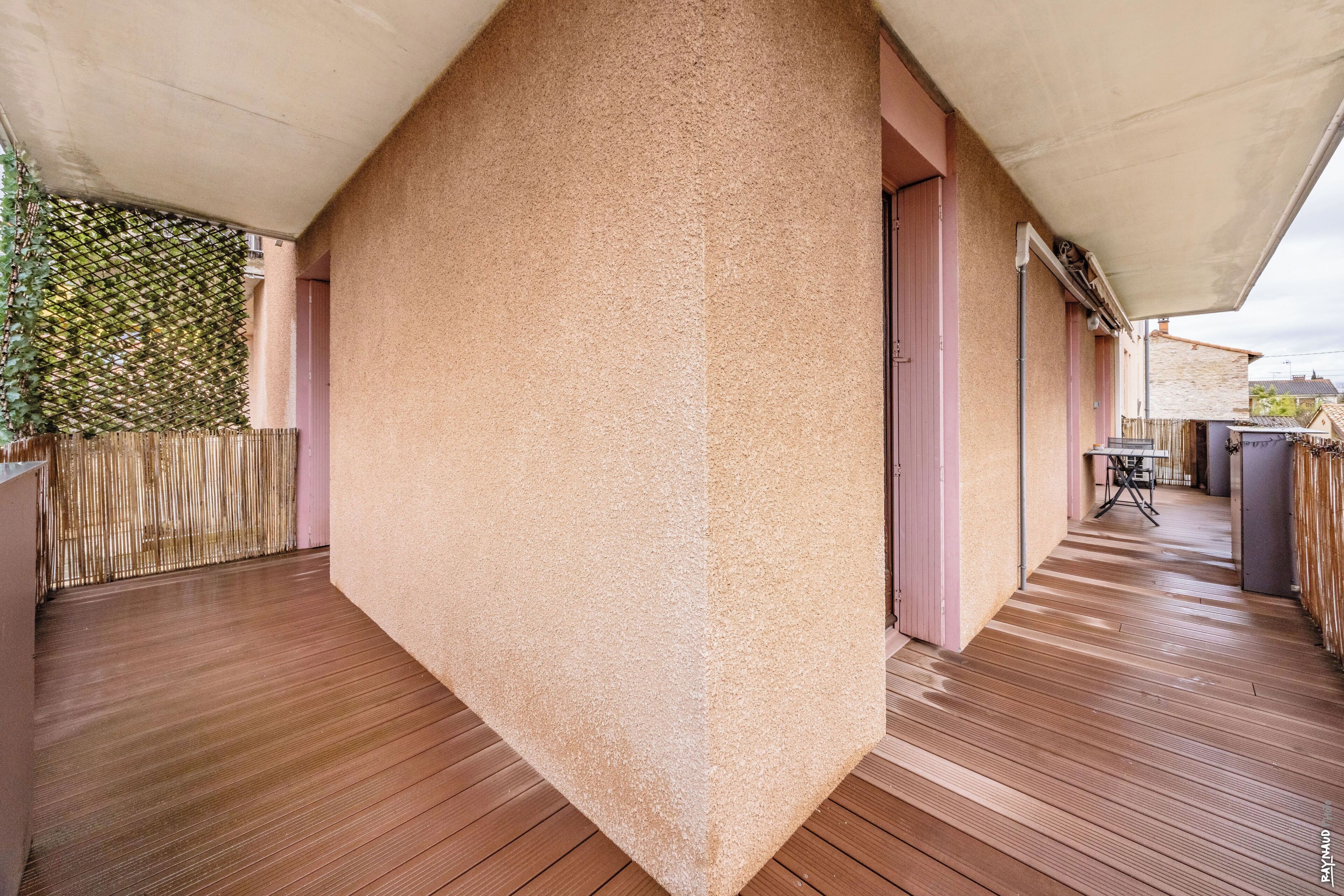 A modern outdoor area with a wooden deck, a textured wall, and a covered seating area.