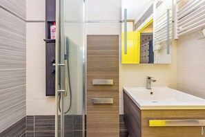 A modern bathroom with a glass shower enclosure, a white sink, and a yellow cabinet.