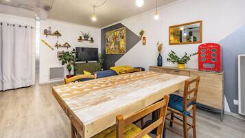 A modern living room with a wooden dining table, yellow cushions, and a red ice cream vending machine.