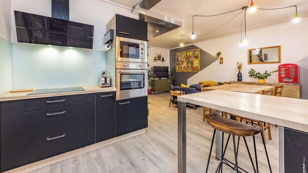Une cuisine moderne dotée d’appareils électroménagers intégrés, un coin repas avec des tabourets et un espace de vie comprenant un canapé et une machine à café.