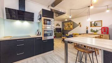 A modern kitchen with built-in appliances, a dining area with stools, and a living space with a sofa and a coffee machine.