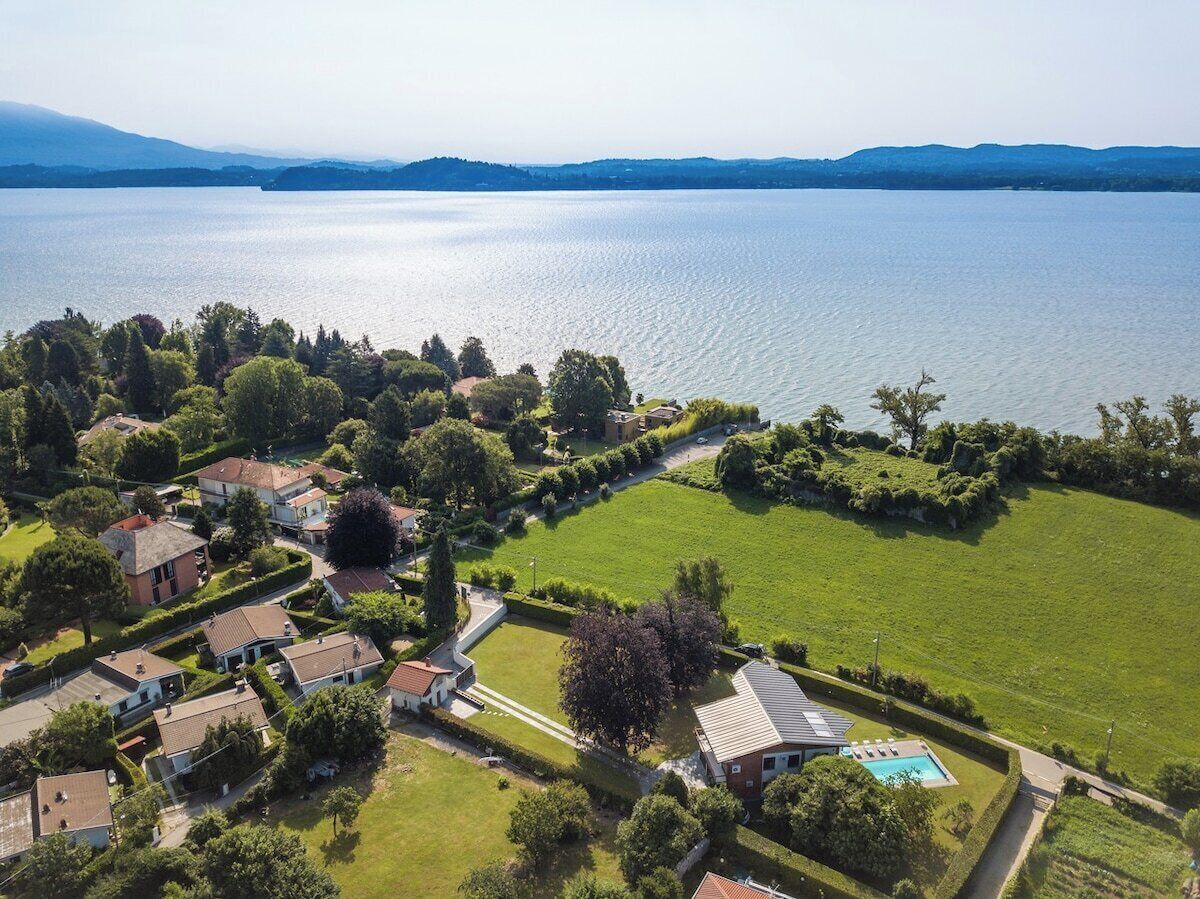 Ovenfra ses et boligområde med huse, en swimmingpool og et stort vandområde i baggrunden.