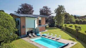 Een modern huis met een zwembad, een overdekt terras en een verzorgd gazon.