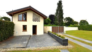 Een modern huis met twee verdiepingen en een plat dak, met een ruitpatroon op de bovenste muur en een verharde oprit naar de ingang.