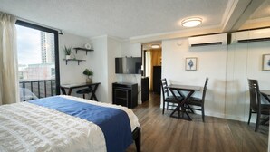 Ett hotellrum med en stor säng, ett skrivbord, en stol, en TV och en balkong med utsikt över staden.