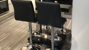 A modern kitchen with a central island, black bar stools, a microwave, and a stainless steel sink.