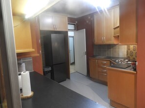 A compact kitchen with wooden cabinets, a black countertop, and a stainless steel refrigerator. - Stunning Panoramic View Swimming Pool 3-bedroom Apartment in the Luxury of Eros. (Windhoek)