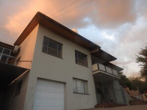 A two-story residential building with a garage, a balcony, and a staircase leading to an upper level. - Stunning Panoramic View Swimming Pool 3-bedroom Apartment in the Luxury of Eros. (Windhoek)