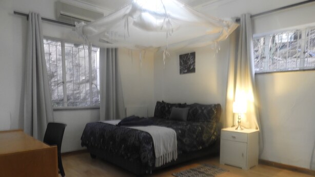 Una camera da letto con un letto, una sedia, un comodino con una lampada e una finestra con tende.