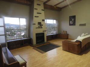A spacious living room with a fireplace, wooden flooring, a sofa, and large windows offering a view of the city. - Stunning Panoramic View Swimming Pool 3-bedroom Apartment in the Luxury of Eros. (Windhoek)