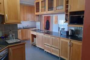 A kitchen with wooden cabinets, a microwave, a kettle, and a tiled backsplash.