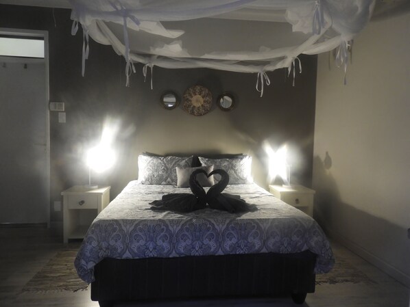 A bedroom with a bed, two bedside lamps, a wall clock, and a mirror.