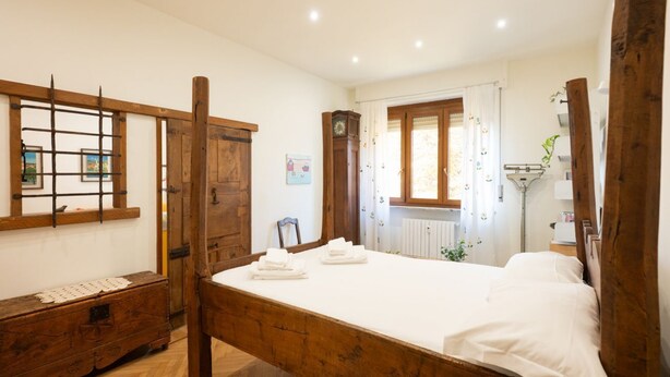 A bedroom with a wooden bed, a wooden dresser, a mirror, a clock, and a window with curtains. - COLLINA E LUCE - Relax, terraces and green view minutes from center (Torino)