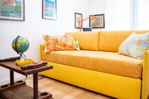 Un sofá amarillo con cojines estampados, un globo terráqueo sobre una mesa de madera y cuadros en la pared.