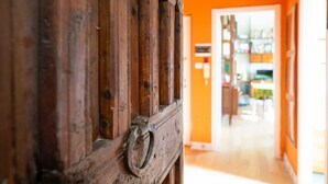 A wooden door with a metal handle, leading to a room with orange walls and a visible dining area in the background. - COLLINA E LUCE - Relax, terraces and green view minutes from center (Torino)