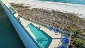 A pool area with blue lounge chairs, a view of the beach, and a sandy area with a fence. - Beachfront-Dog Friendly-Panoramic Gulf View (Orange Beach)