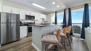 A modern kitchen with stainless steel appliances, a central island with bar stools, and a view of the ocean through large windows. - Beachfront-Dog Friendly-Panoramic Gulf View (Orange Beach)
