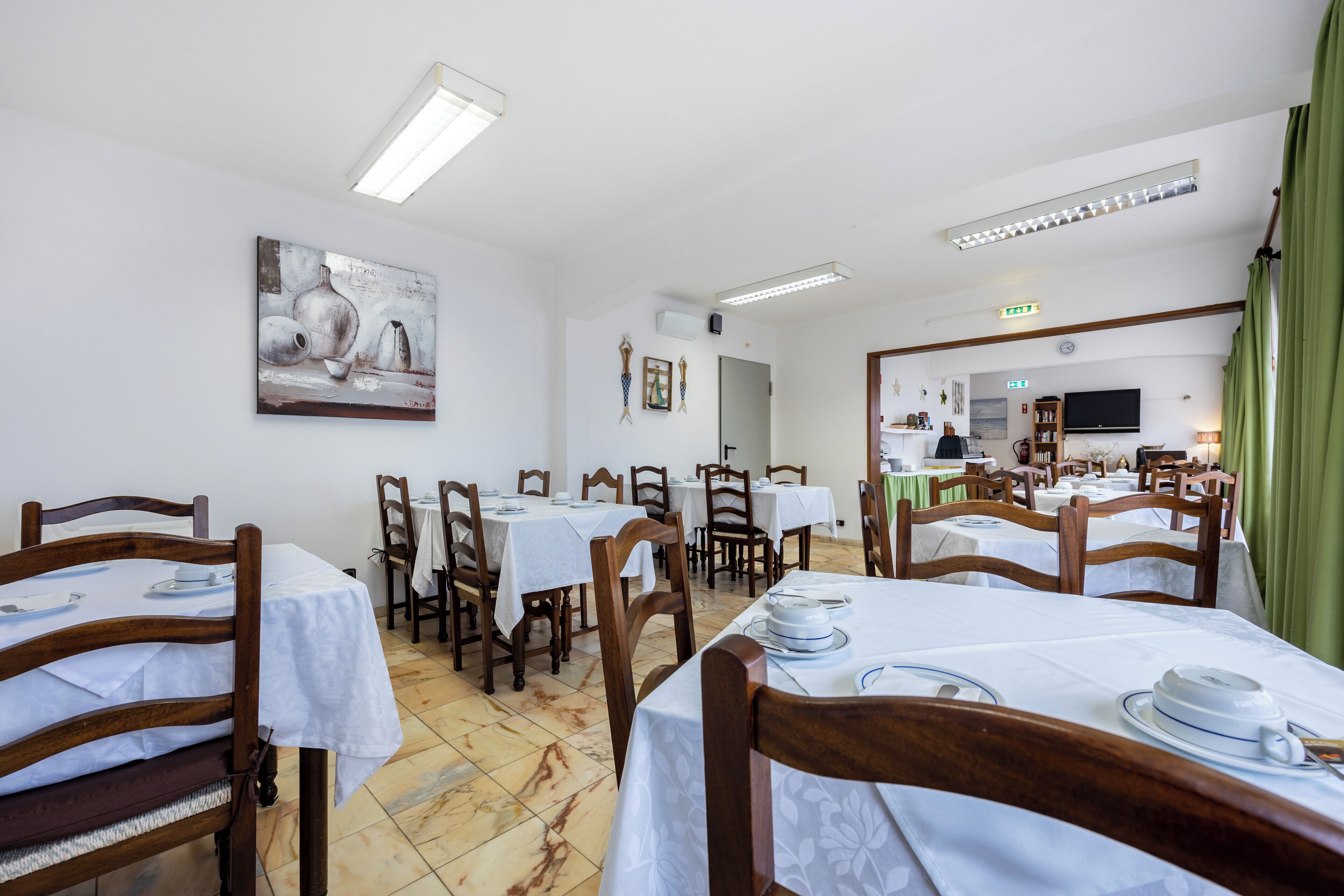 A dining area with multiple tables and chairs, white tablecloths, and a painting on the wall.