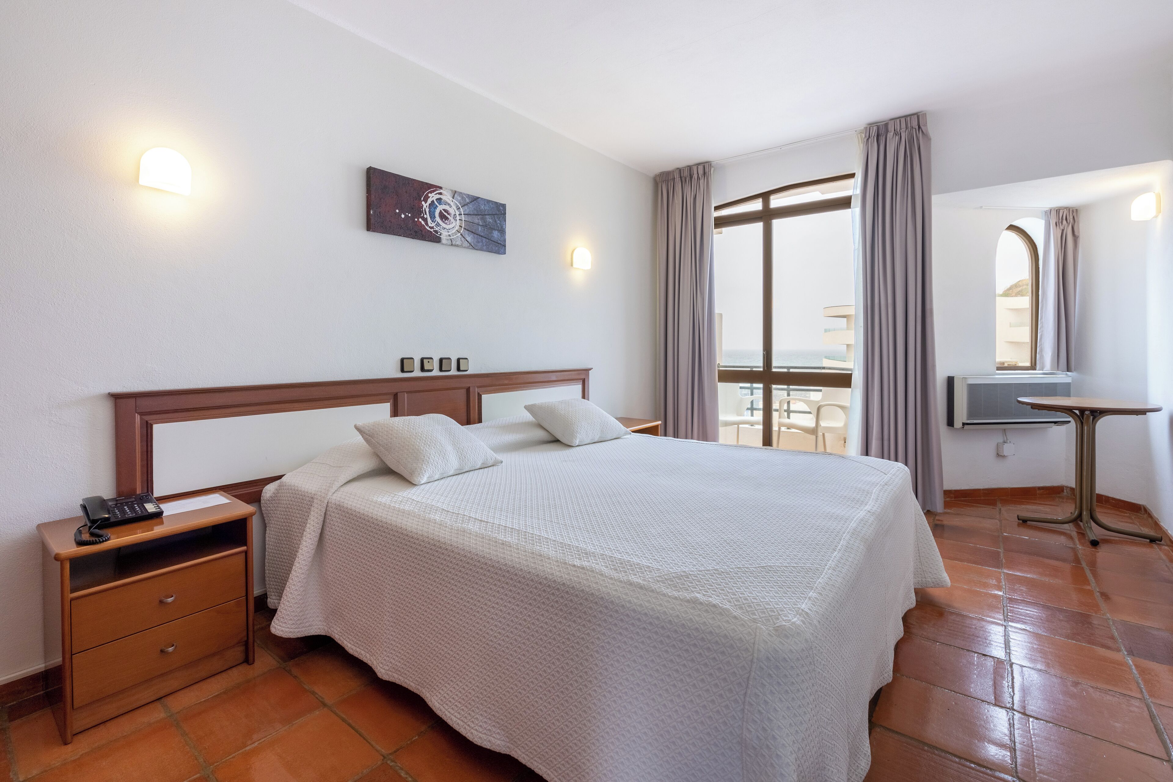Habitación de hotel con una cama grande, una mesita de noche, un escritorio y una ventana con cortinas.