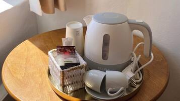 Ein Tisch mit einem weißen Wasserkocher, einer weißen Tasse, einem weißen Ladegerät und einem gewebten Korb mit Gegenständen darin.
