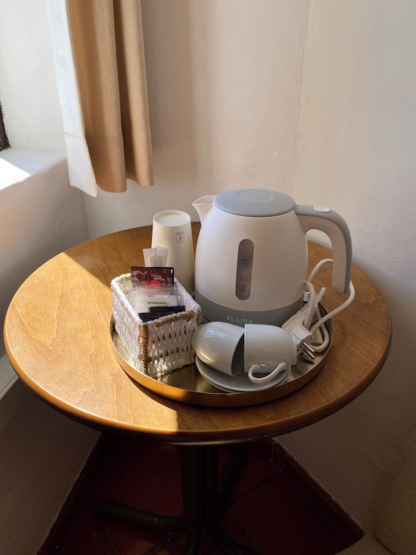 A table with a white kettle, a white mug, a white charger, and a woven basket with items on it.