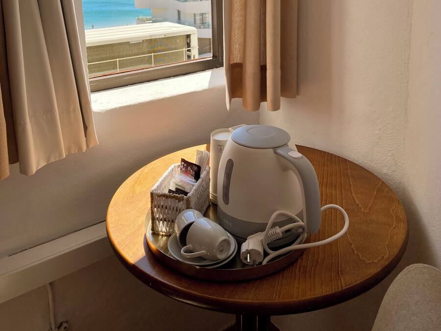 Habitación de hotel con vista al mar, una mesa con hervidor, tazas y una cesta de objetos.