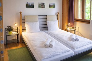 A double bed with white linens and rolled towels, two bedside tables with lamps, a green rug, and a window with curtains. - Ca Brunella 2 Lake Maggiore View Terrace for Four (Cugnasco-Gerra)