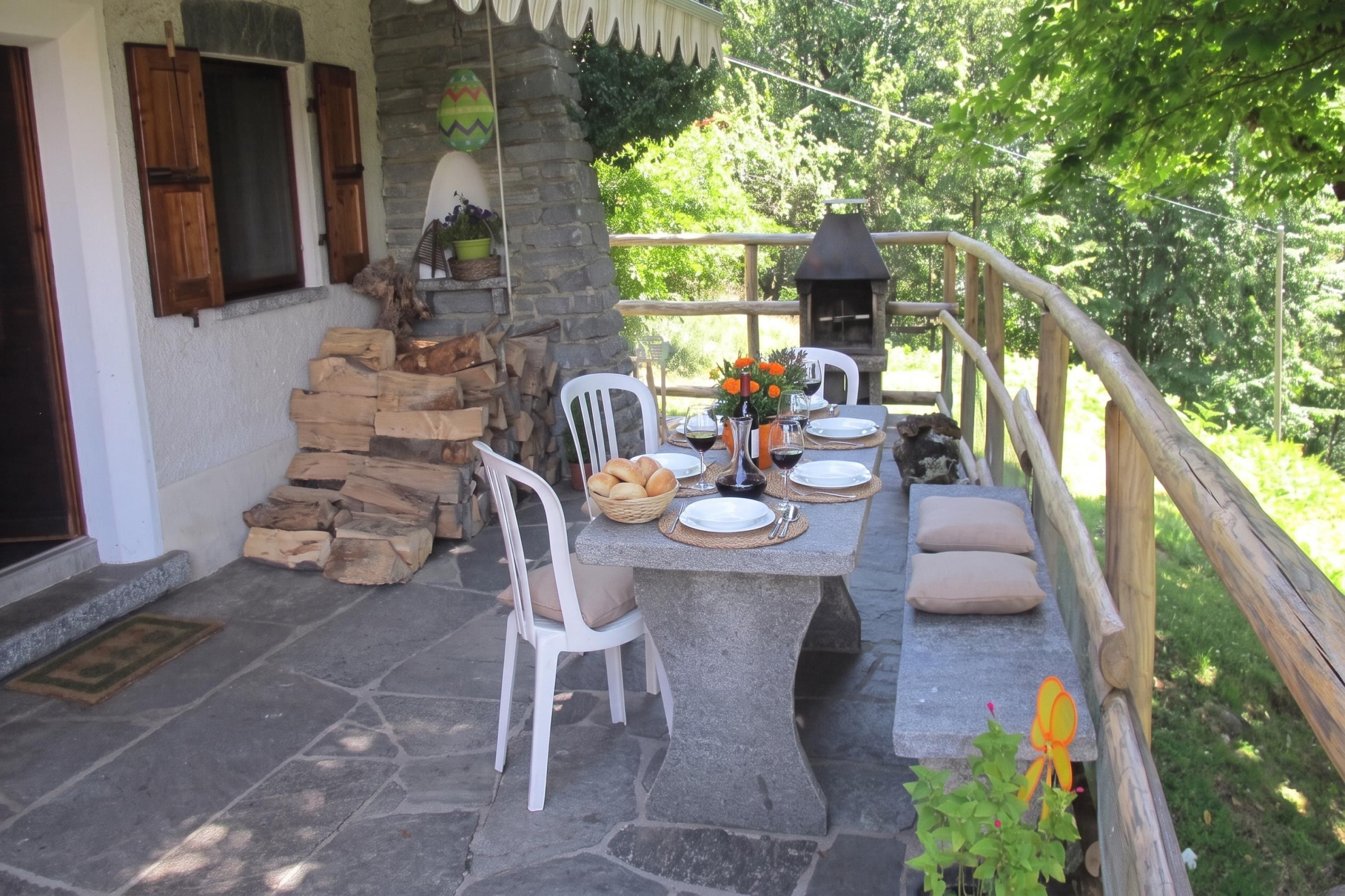 An outdoor patio with stone flooring, a stone table set for dining, white chairs, and a wooden fence.