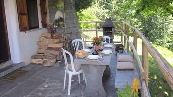 An outdoor patio with stone flooring, a stone table set for dining, white chairs, and a wooden fence.