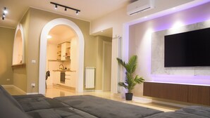 Un salon moderne avec un grand canapé gris, un téléviseur à écran plat fixé au mur et une plante en pot.