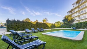 Ein Poolbereich mit grünem Kunstrasen, mehreren Liegestühlen und einem Gebäude mit Balkonen im Hintergrund.