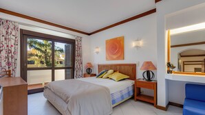 Ein Schlafzimmer mit Bett, Nachttischen, Schreibtisch, Stuhl, Fenster mit Vorhängen und einem Wandspiegel.