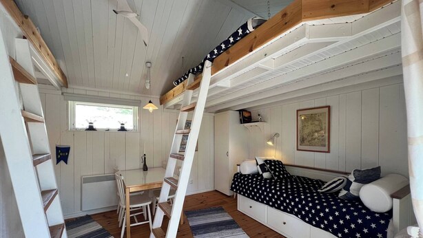 A cozy cabin interior with a wooden staircase, a dining area with a table and chairs, a sofa with star-patterned bedding, and a framed map on the wall. - Room-archipelago Cottage is Utö (Uto)