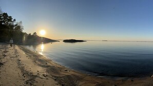 A calm lake with a clear sky and a person walking on the shore. - Room-archipelago Cottage is Utö (Uto)