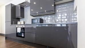 Een moderne keuken met grijze kastjes, een roestvrijstalen afzuigkap en een betegelde achterwand.