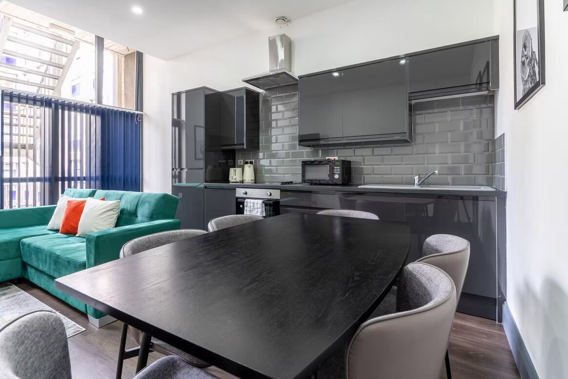 Une cuisine moderne avec des meubles de couleur sombre, un plan de travail noir et un coin repas comprenant une table noire et des chaises grises.