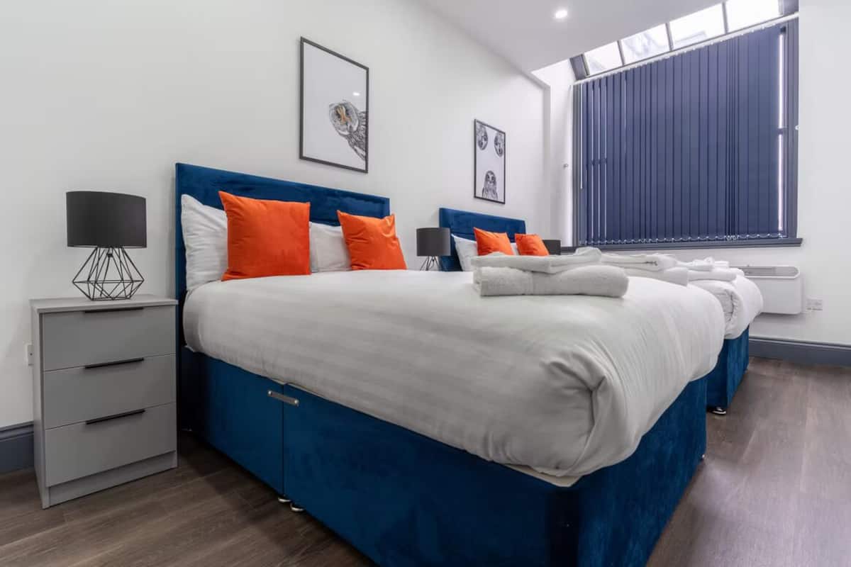 Une chambre d’hôtel moderne avec un grand lit, deux tables de chevet, une lampe et une fenêtre avec des stores.