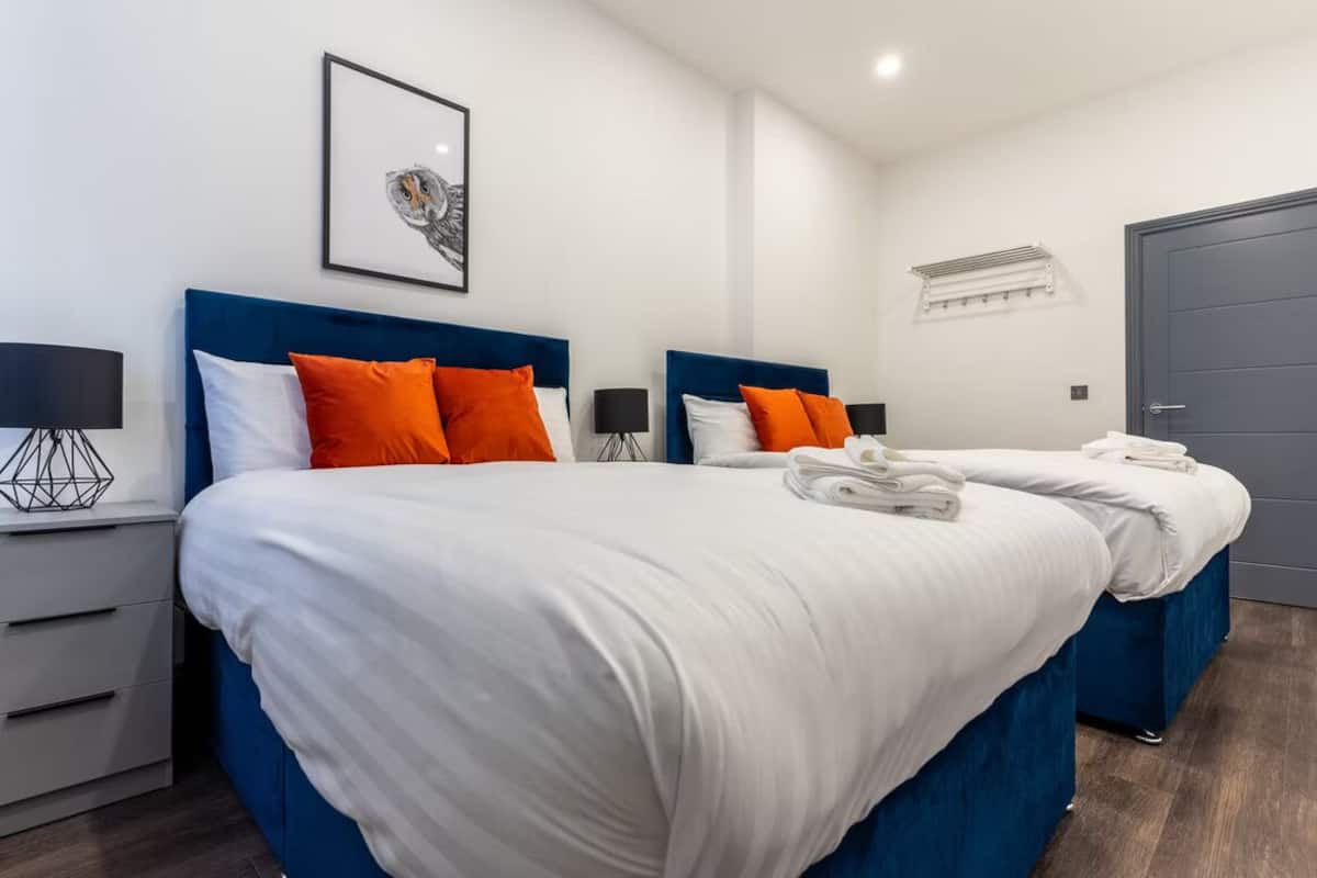 Une chambre d’hôtel avec deux lits, du linge de lit blanc, des têtes de lit bleues et une œuvre d’art encadrée au mur.