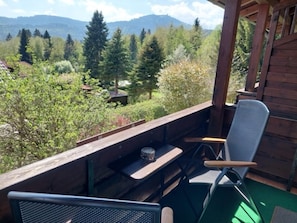 A wooden deck with a metal chair and a table, overlooking a forested area with mountains in the distance. - Hotel Haus Anna (Bayerisch Eisenstein)