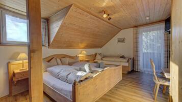 A bedroom with a wooden ceiling, a bed, a bedside table with a lamp, a chair, and a window with curtains.