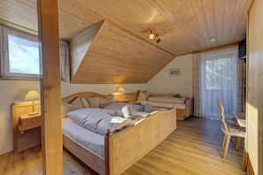 A bedroom with a wooden ceiling, a bed, a bedside table with a lamp, a chair, and a window with curtains. - Hotel Haus Anna (Bayerisch Eisenstein)