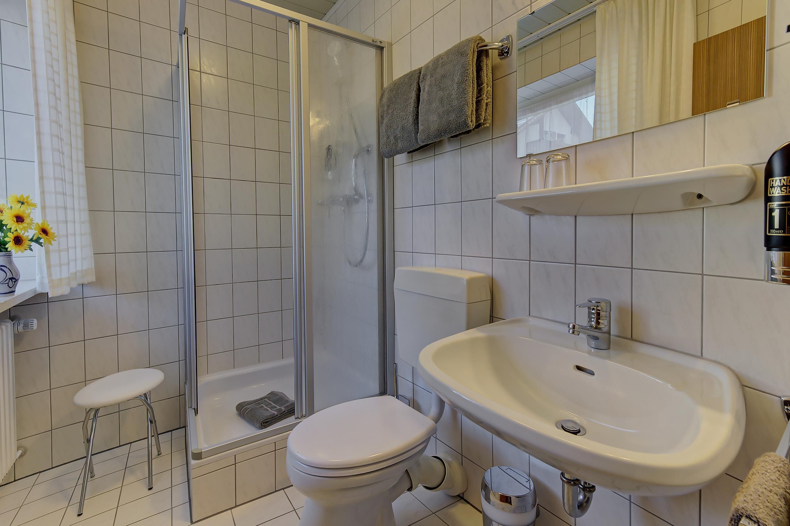 A bathroom with a shower, toilet, sink, and a small stool.
