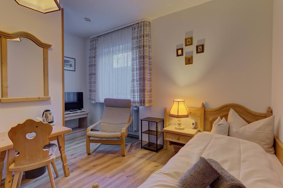 Ein Hotelzimmer mit Bett, Schreibtisch mit Stuhl, Fernseher, Lampe und einem Fenster mit Vorhängen.