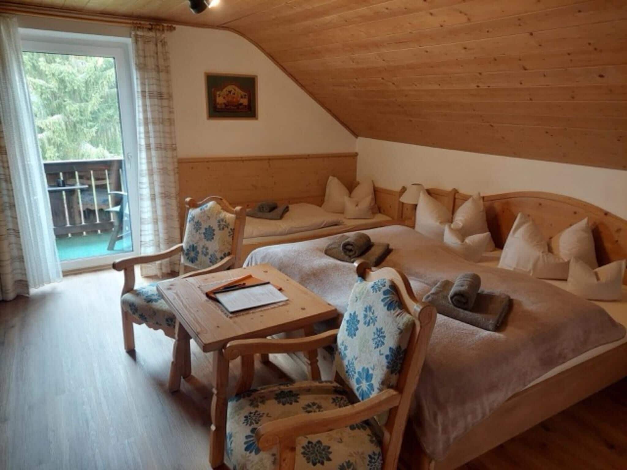 Una habitación acogedora con techo de madera, dos camas con almohadas, una mesa con una silla y vistas al exterior con vegetación.