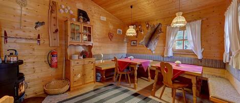 A cozy cabin interior with a wooden interior, a dining area with a red tablecloth, a fireplace, and a bench.