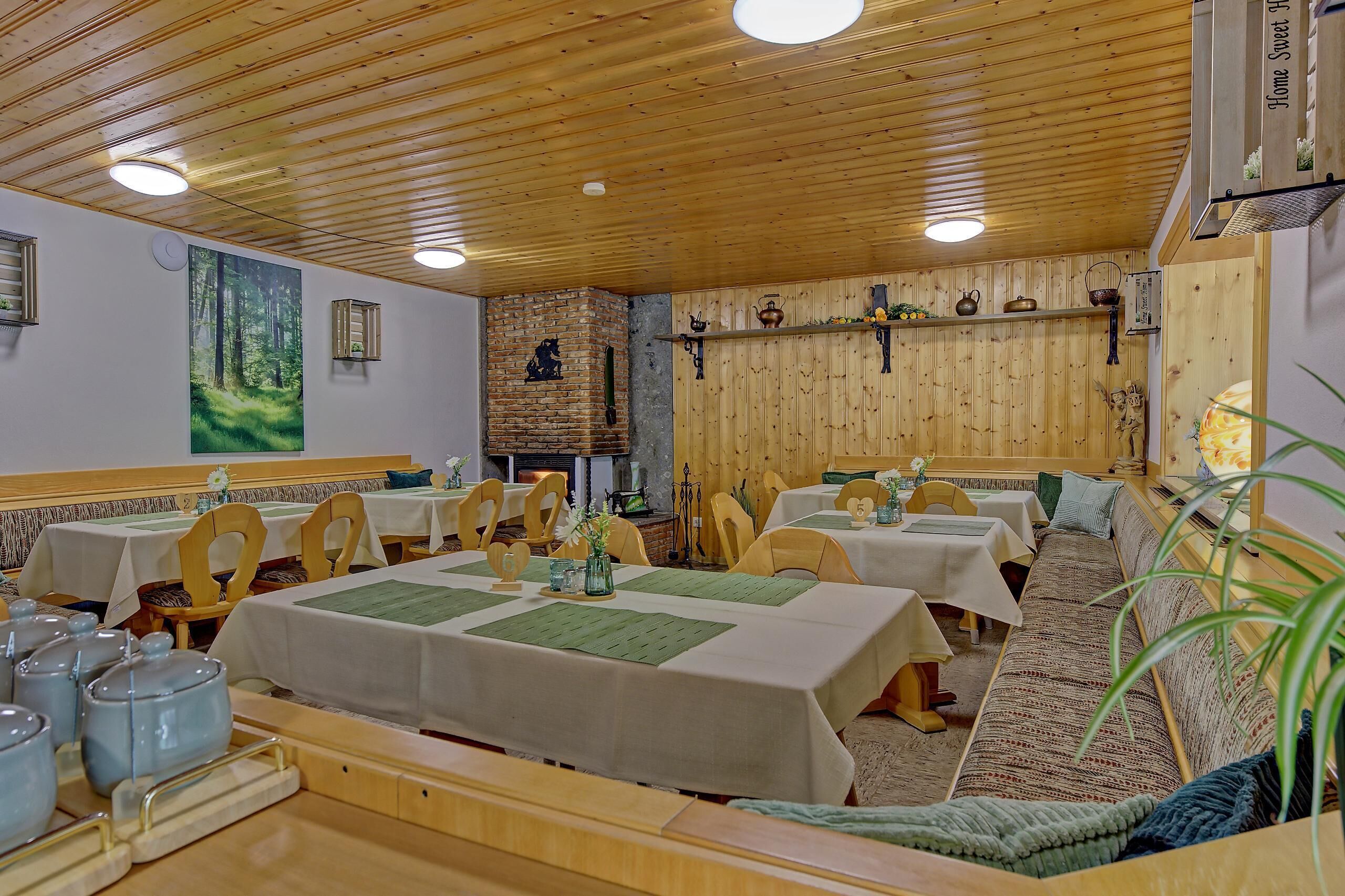Un restaurante con techo y paredes de madera, varias mesas con manteles blancos y una chimenea de ladrillo.