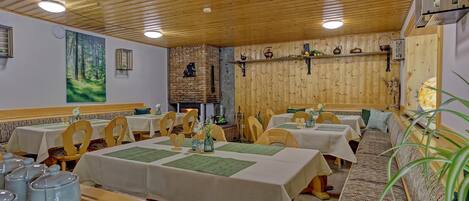 Un restaurante con techo y paredes de madera, varias mesas con manteles blancos y una chimenea de ladrillo.