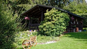 Un'accogliente baita di legno con veranda, circondata da un lussureggiante verde e un carro di legno.