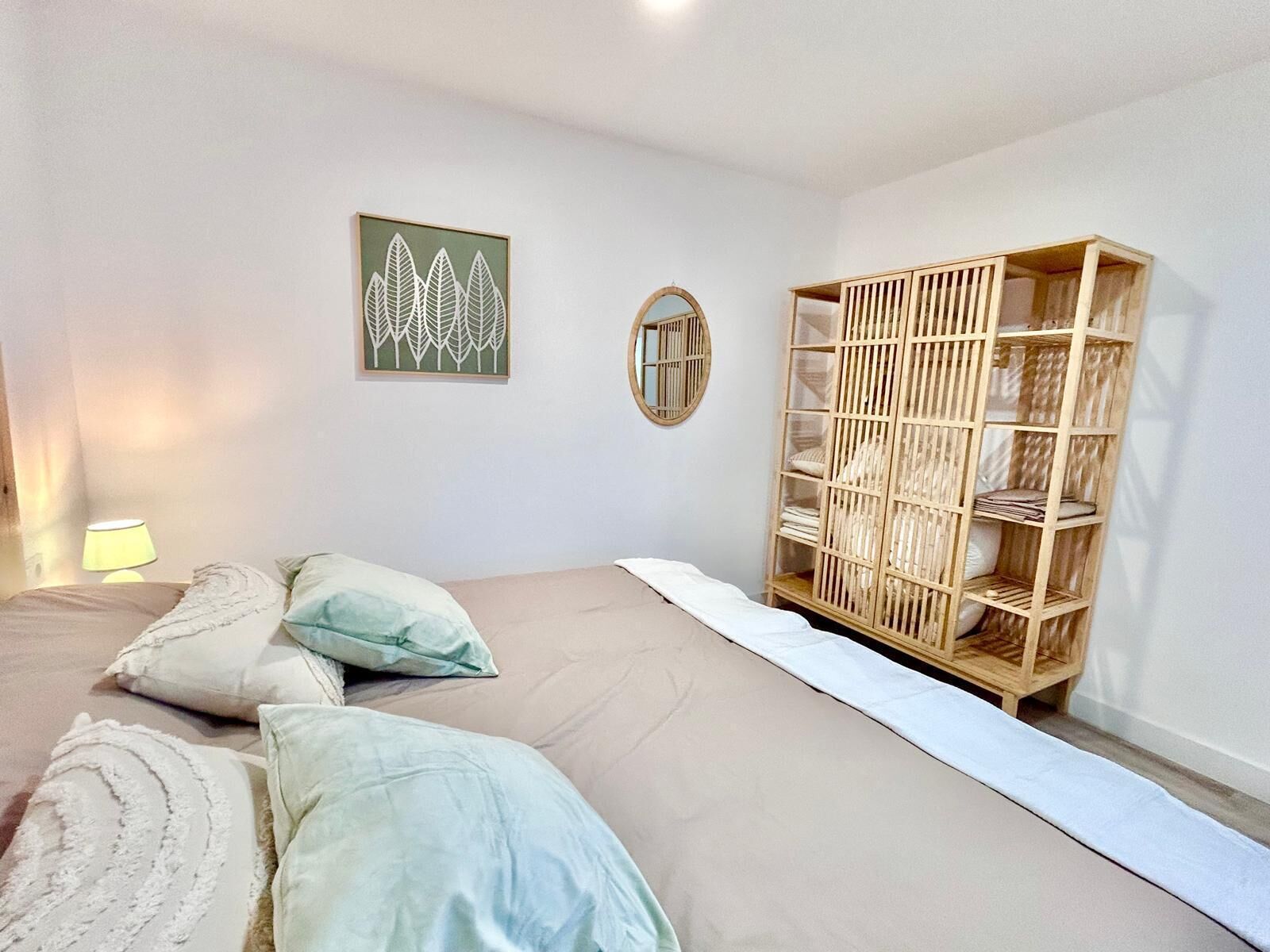 Une chambre à coucher avec un lit, des oreillers, une armoire en bois, un miroir et une œuvre d’art murale.